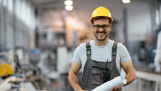 A manufacturing worker in a hard hat with plans for safety-rated components on a factory floor.